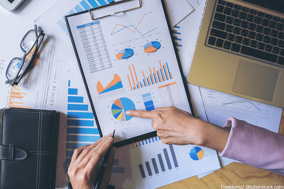 Charts and graphs on a desk with person pointing to a chart